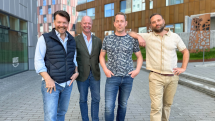 4 men standing outside infront of a building smiling 