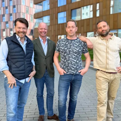4 men standing outside infront of a building smiling 